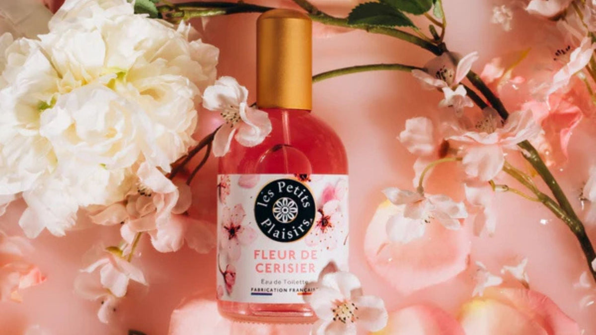 Flacon de l’eau de toilette Fleur de Cerisier des Petits Plaisirs, entouré de fleurs blanches et roses, illustrant un parfum printanier délicat et floral.