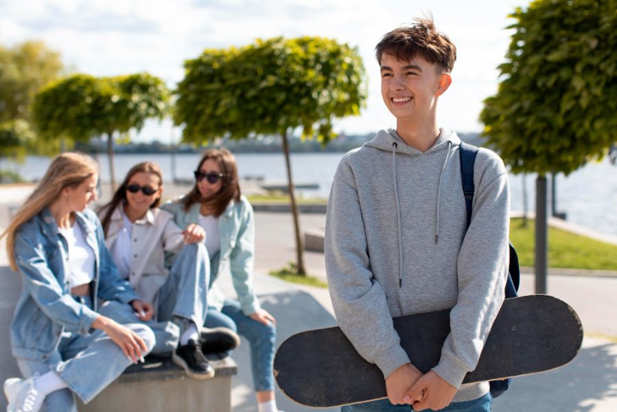 Adolescent souriant tenant un skateboard, entouré de ses amis au bord d’un lac, illustration d’un style de vie jeune et dynamique